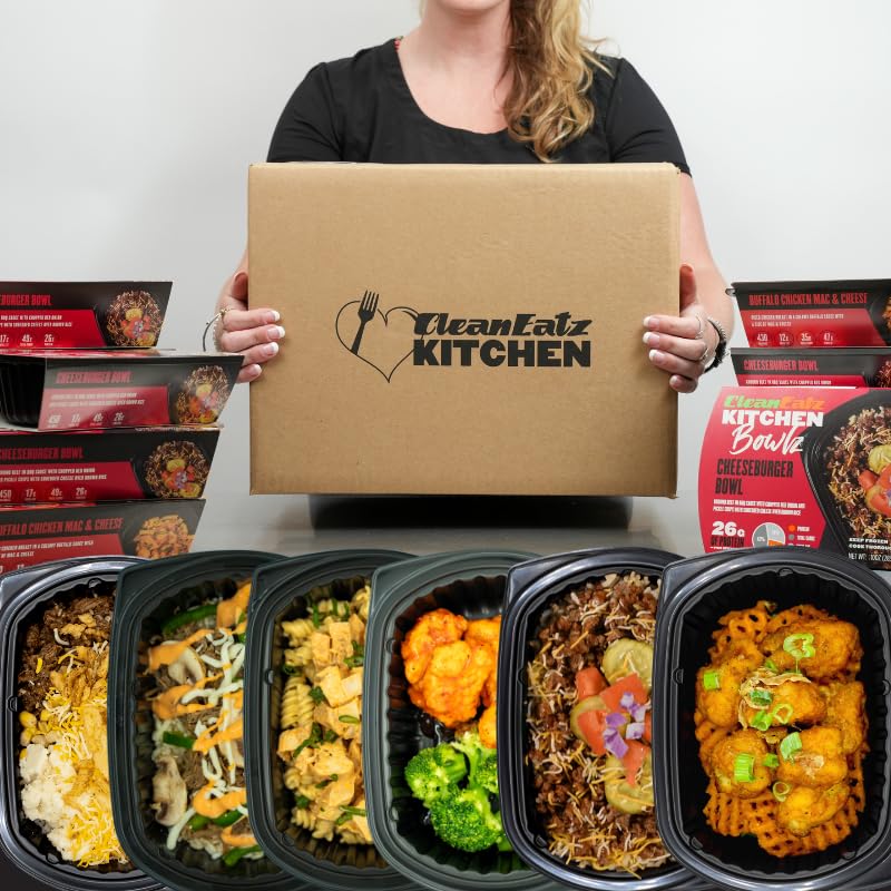 Person holding a Clean Eatz Kitchen box with various prepared meals displayed below.