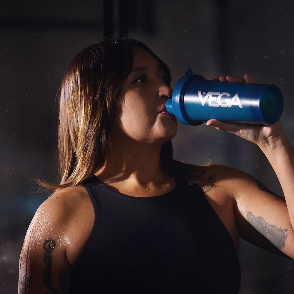 Person drinking from a blue Vega shaker bottle against a dark background