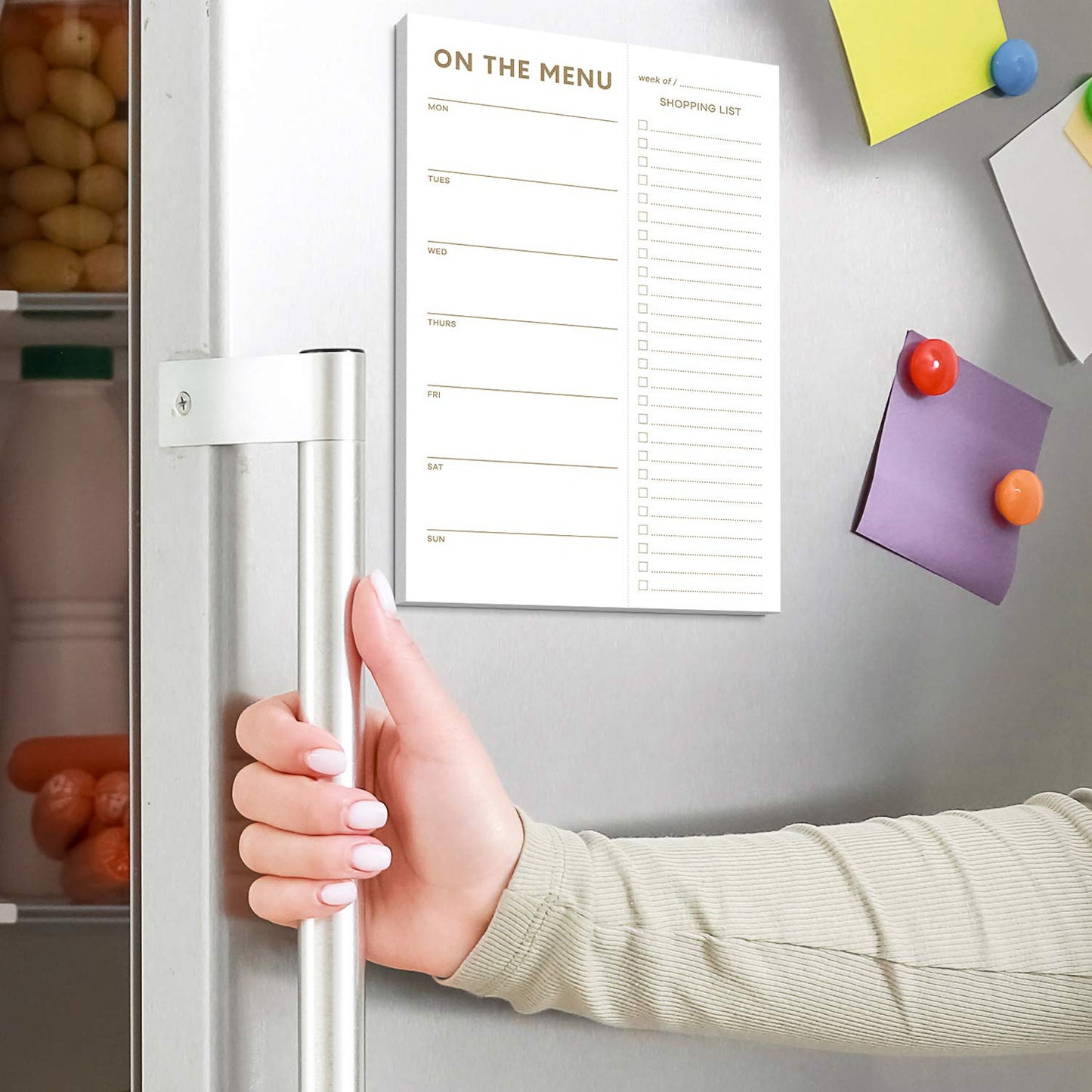 Hand opening a refrigerator door with a magnetic menu board attached.