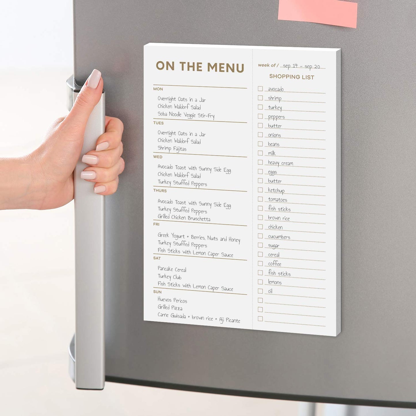 Hand holding a magnetic menu and shopping list on a refrigerator.