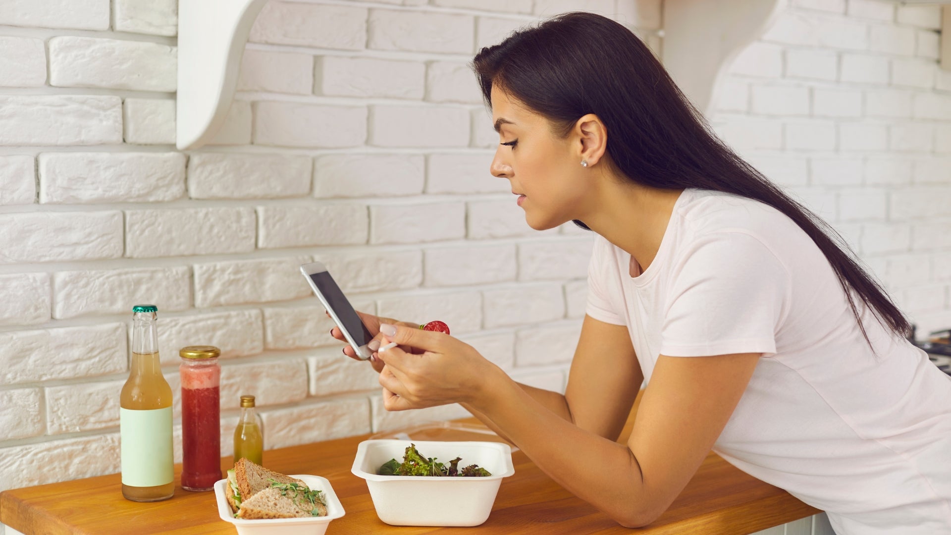 Female customer leaning on a table with a meal and phone, looking at her phone as she reads our FAQ section.