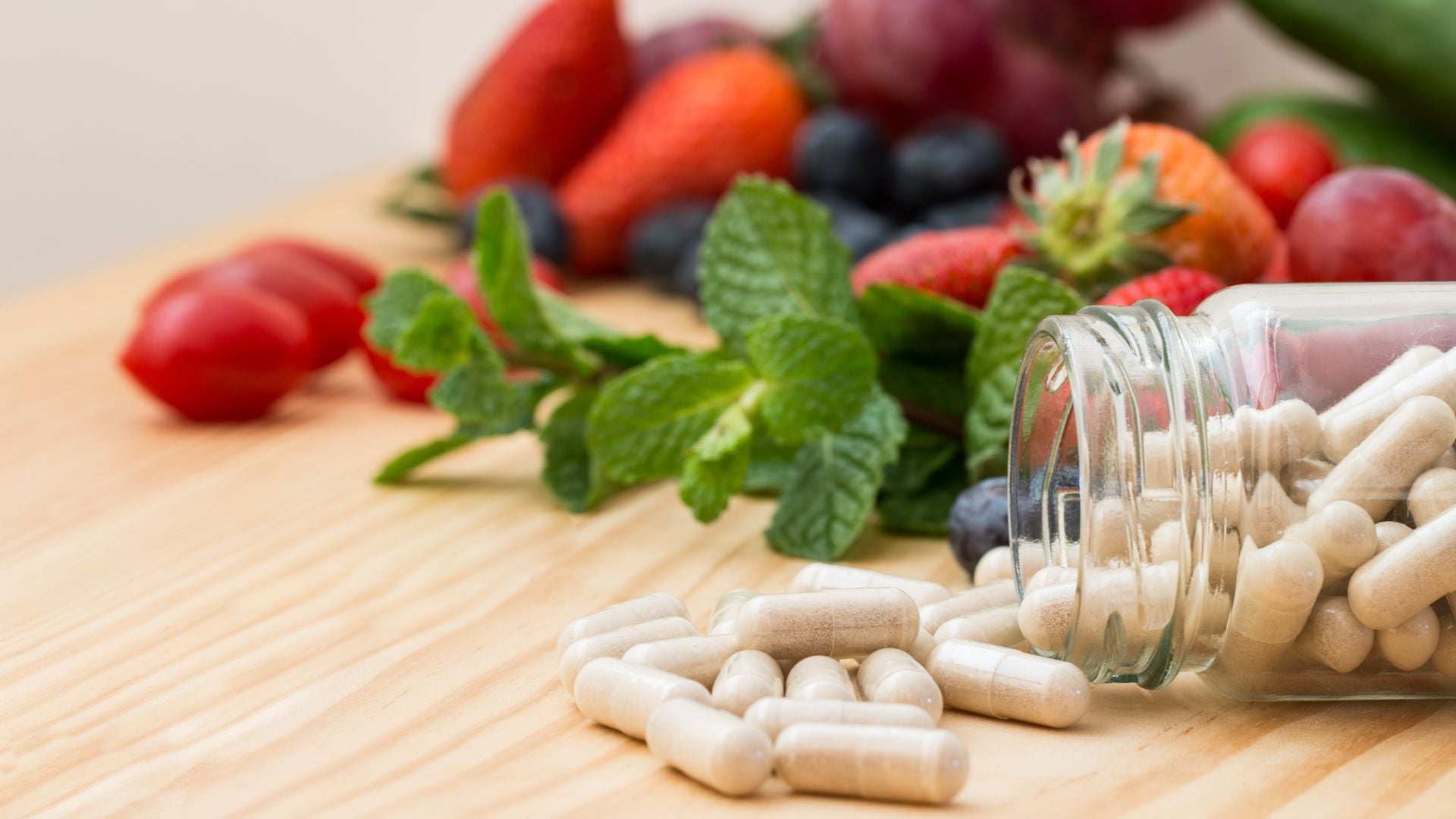 Pills spilling out of a jar with fresh fruits and vegetables on a wooden surface