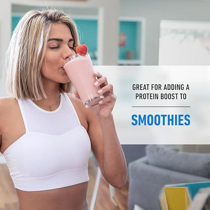 Woman drinking a pink smoothie with a strawberry on top, indoors.