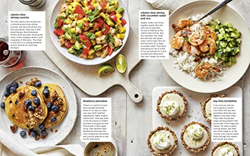 Assorted breakfast dishes including pancakes with blueberries, a salad, and tarts on a wooden surface.