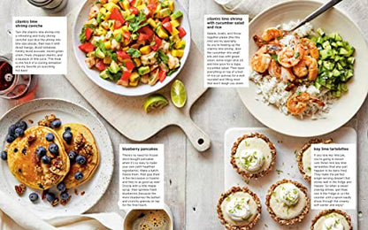 Assorted breakfast dishes including pancakes with blueberries, a salad, and tarts on a wooden surface.