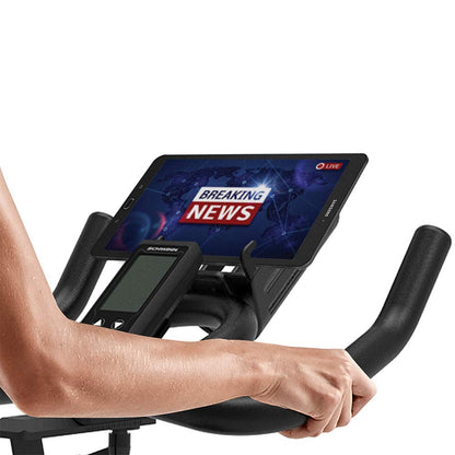 Person using a fitness machine with a tablet displaying 'Breaking News' on the screen.