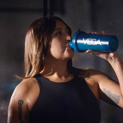 Person drinking from a blue Vega shaker bottle against a dark background