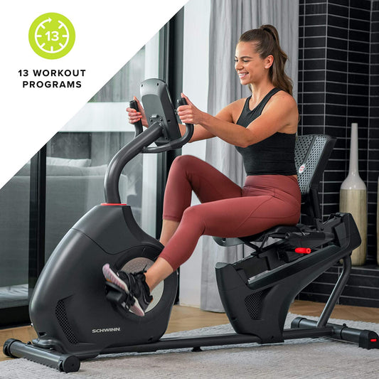 Woman exercising on a Schwinn recumbent bike in a home setting with '13 Workout Programs' text.