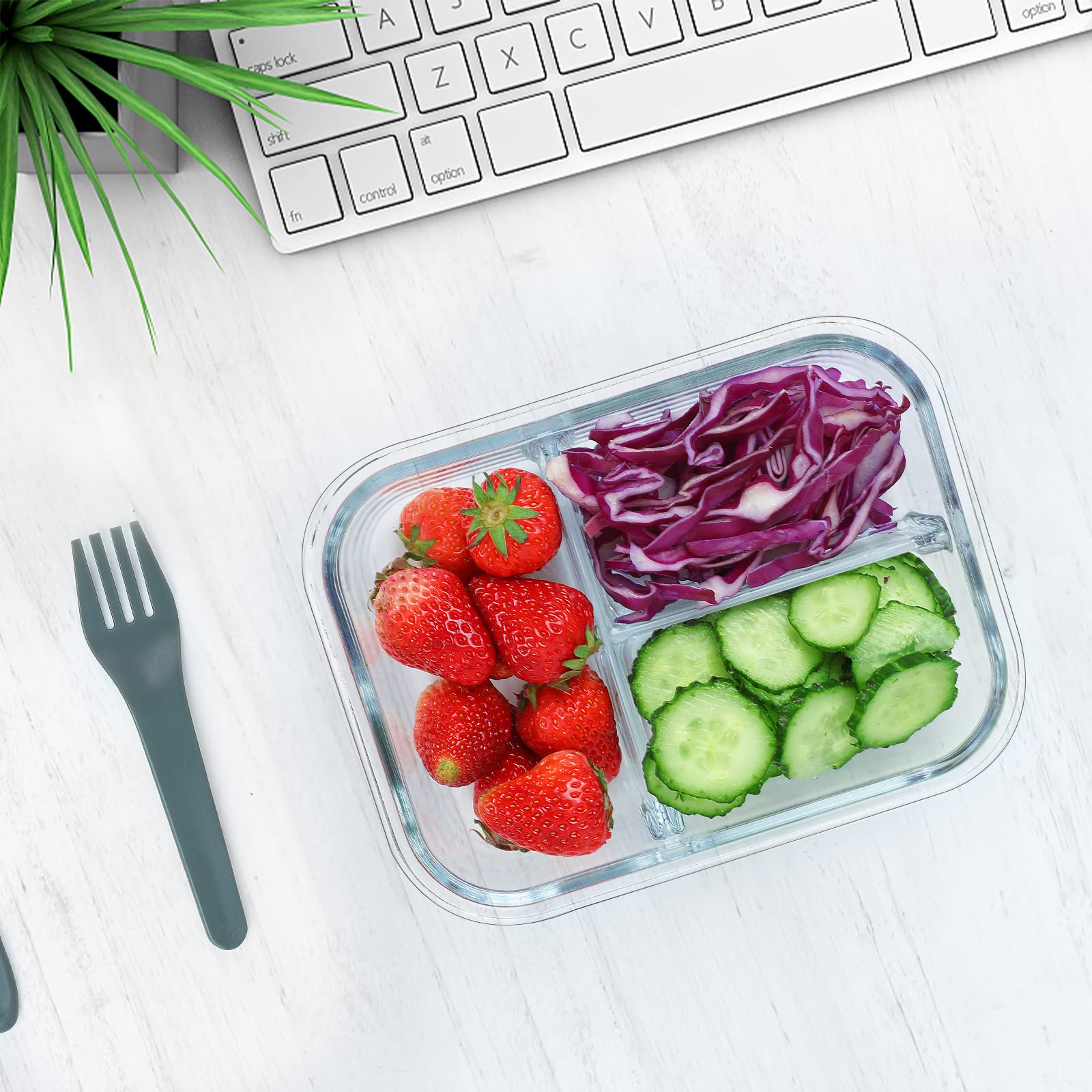 Container of strawberries, red cabbage, and cucumbers on a white surface with a keyboard and plant in the background.