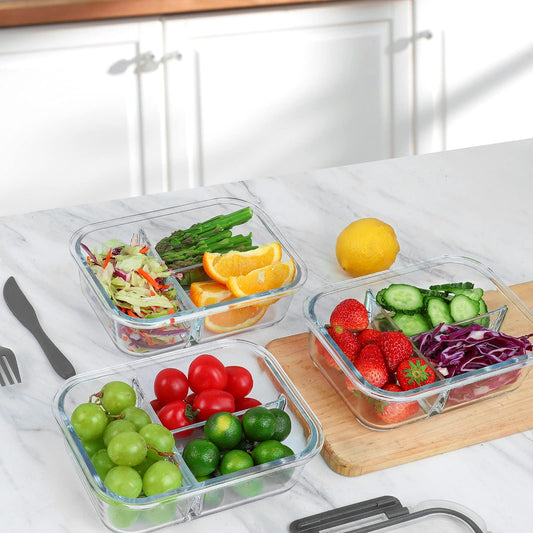 Glass food containers with compartments filled with fruits and vegetables on a kitchen counter.