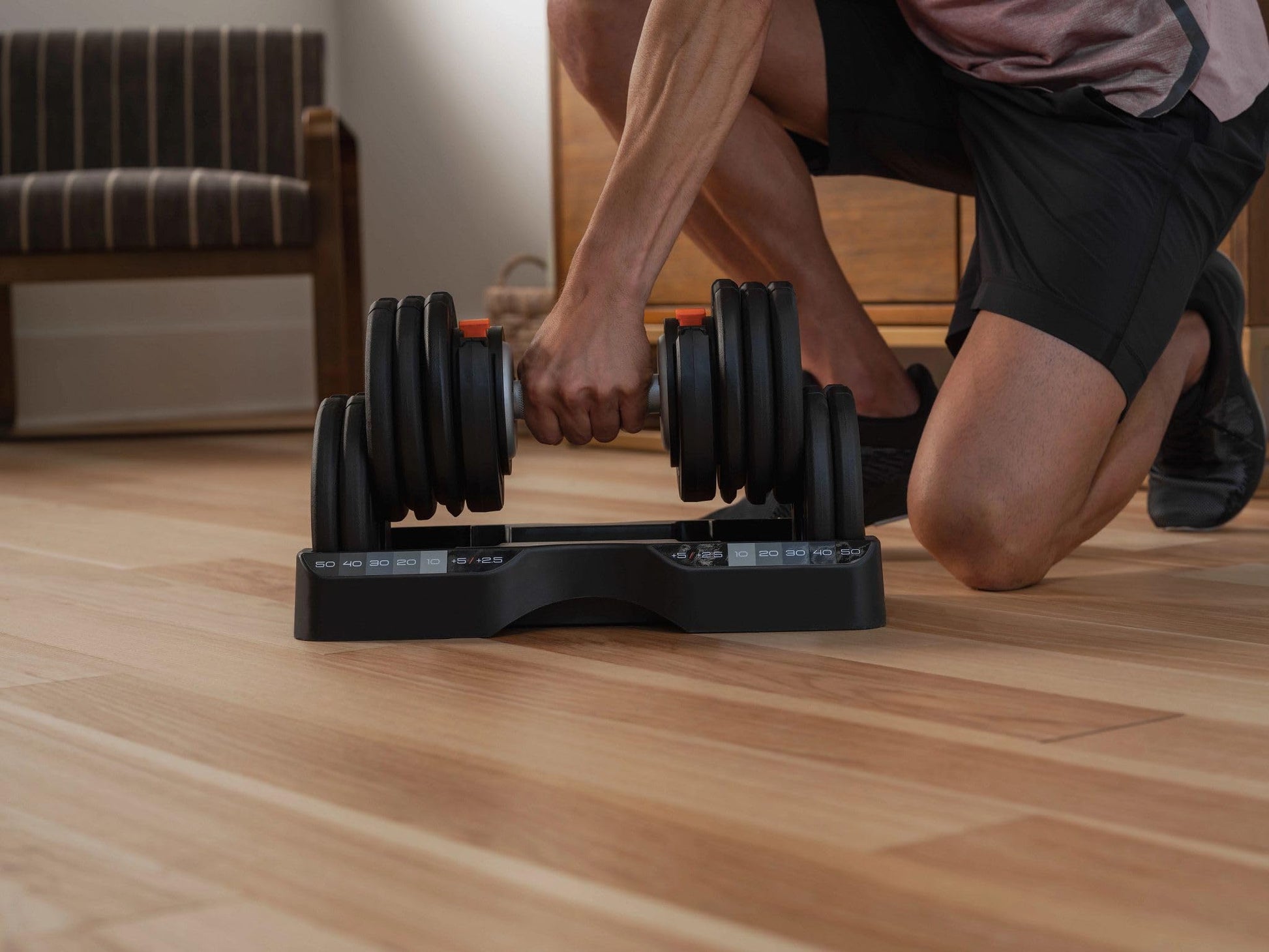 Person adjusting a dumbbell set on a wooden floor