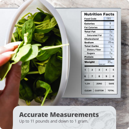 Digital scale with a bowl of spinach and nutrition facts display on a marble surface.
