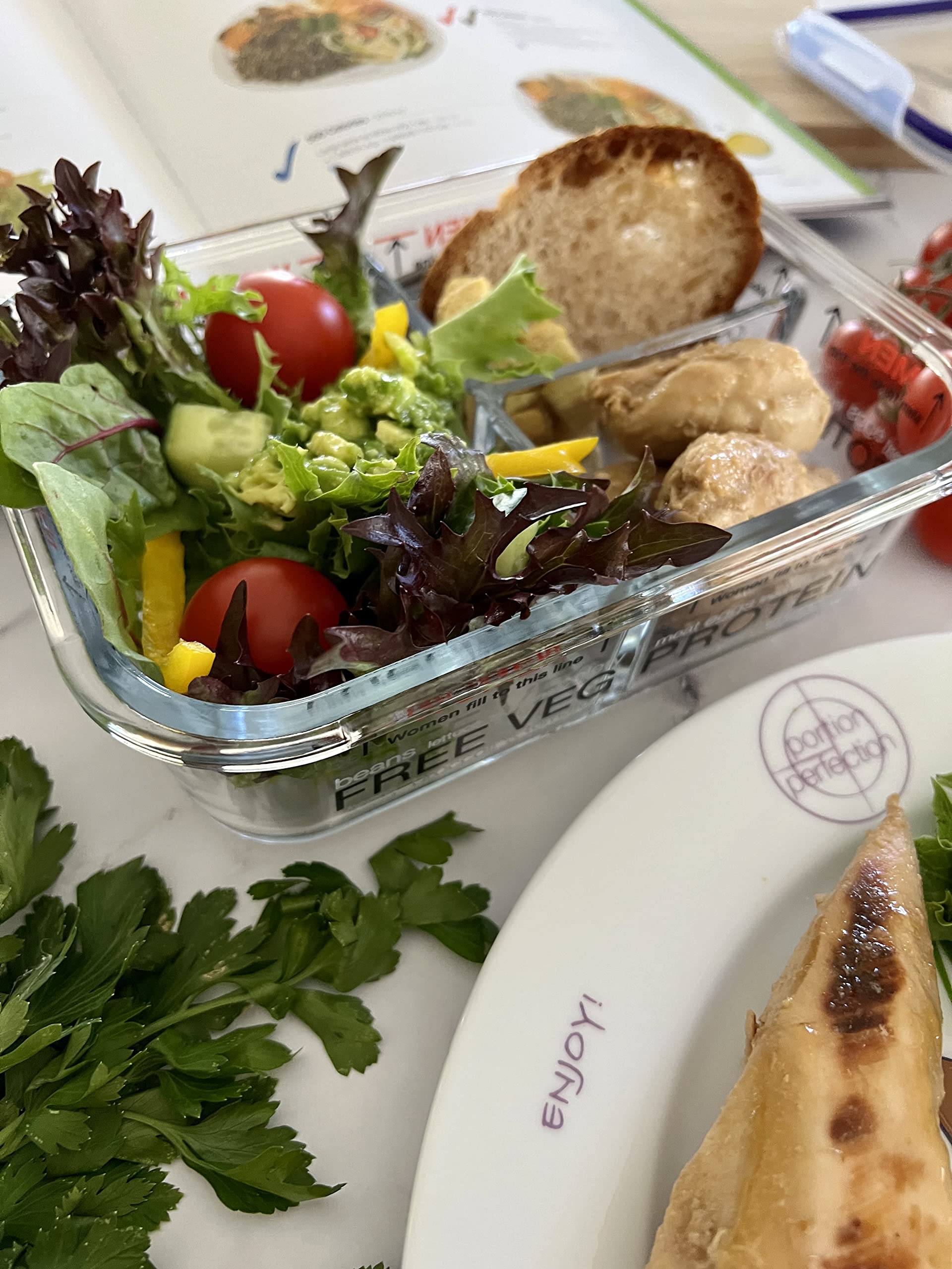 Glass container of salad with bread and crackers on a table with a plate and additional food items.