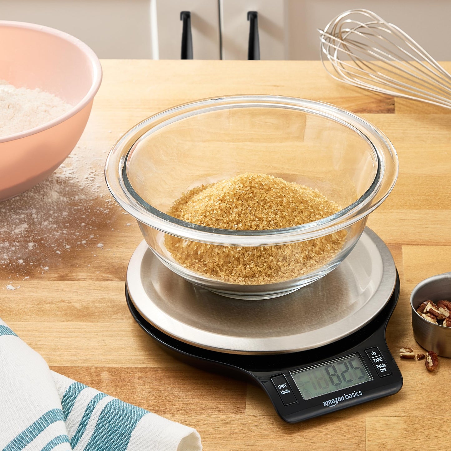Glass bowl with brown sugar on a digital kitchen scale on a wooden countertop.
