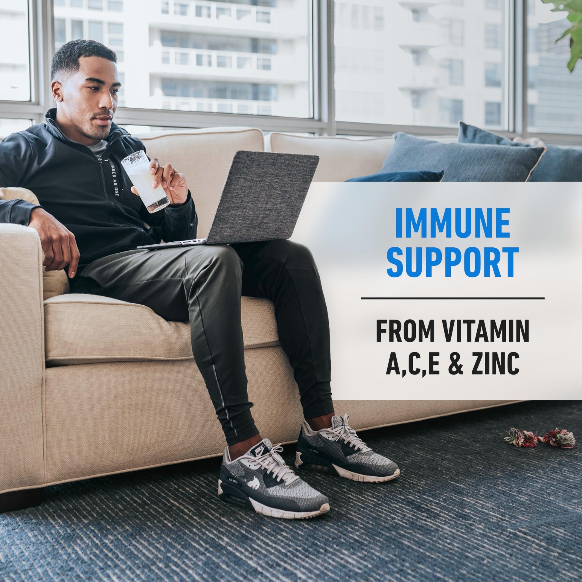 Man sitting on a couch with a laptop, holding a supplement, with text about immune support and vitamins.