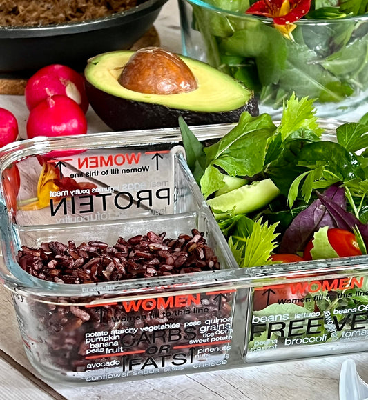 Container of black rice with a salad and avocado on a table