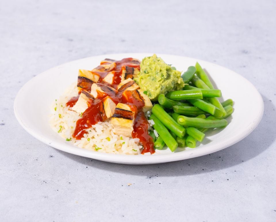 Plate of food with rice, vegetables, and a sauce on a light gray background