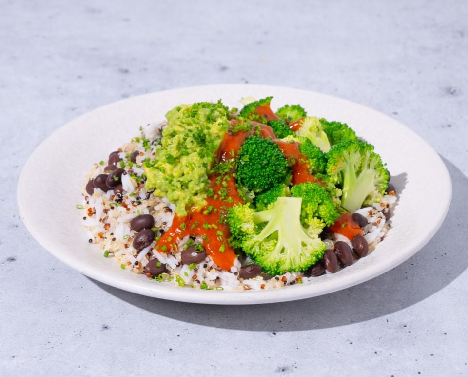 Plate of salad with broccoli, guacamole, and other ingredients on a light gray background