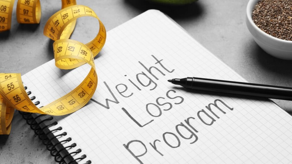 Notebook with weight loss program written on it beside measuring tape and chia seeds