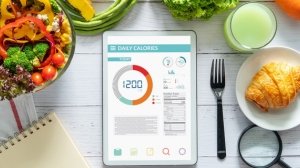 Digital tablet showing daily calorie tracking alongside healthy foods and a food journal
