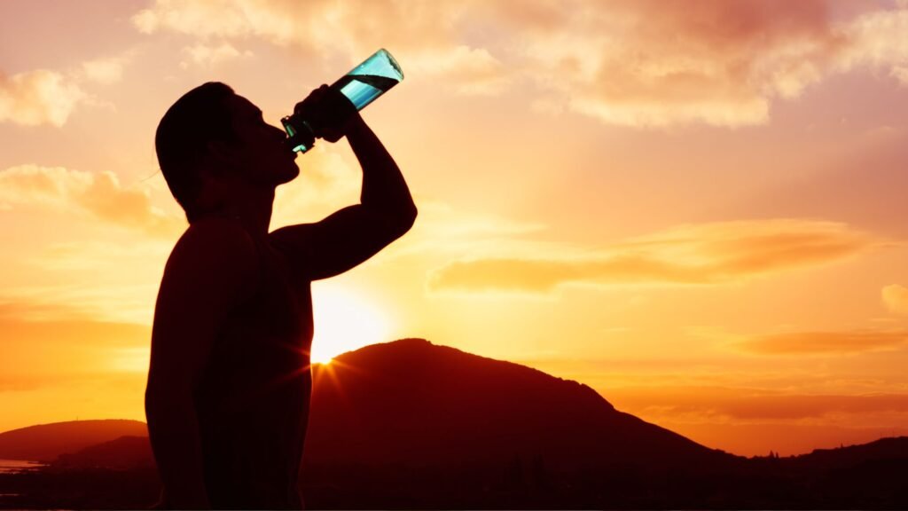 Athlete drinking water or creatine supplement after workout at sunset