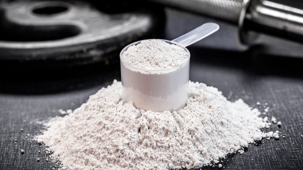Scoop of creatine powder with gym equipment in background