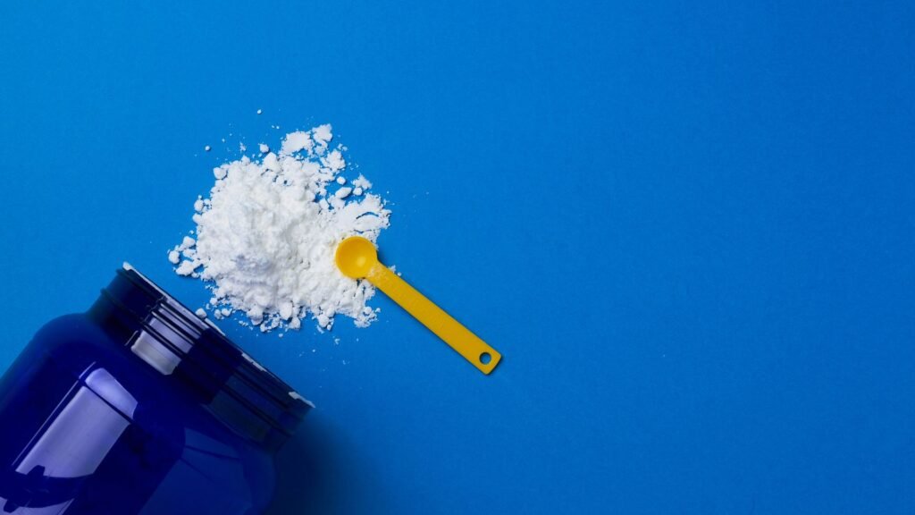 Creatine powder with yellow measuring scoop on blue background