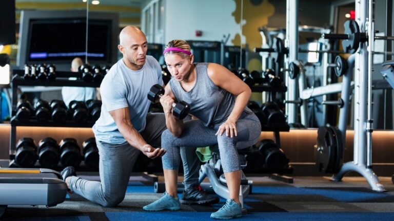 Personal trainer coaching a woman with dumbbells in a gym