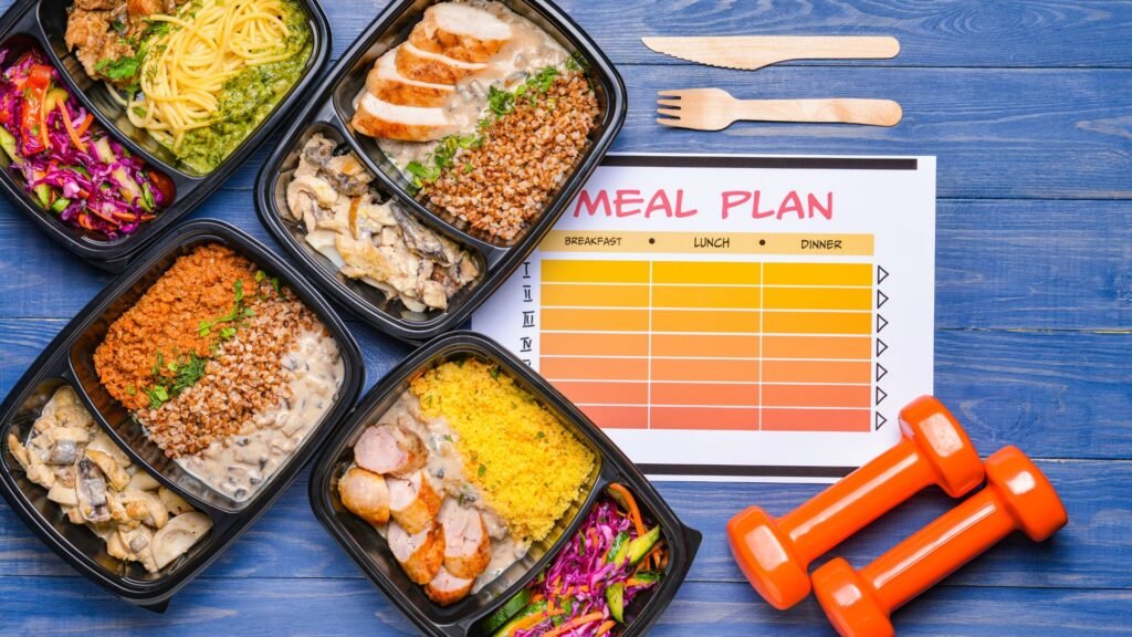 Healthy pre-packaged meal containers with a meal plan chart and dumbbells on a blue table
