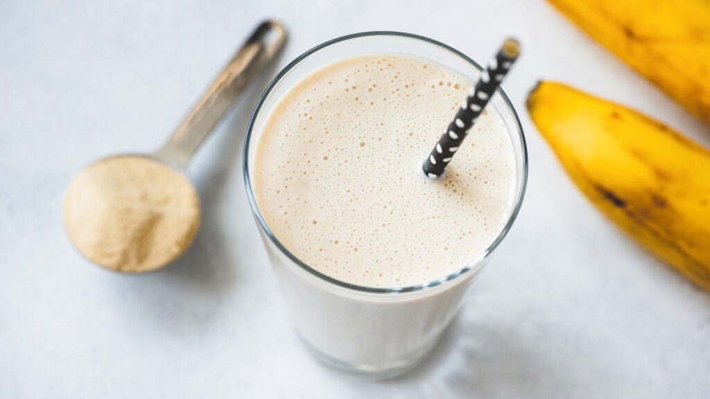 Glass of protein shake with scoop of protein powder and bananas