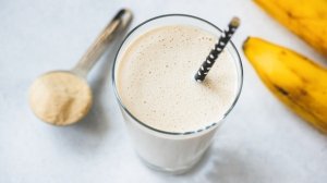 Glass of protein shake with scoop of protein powder and bananas