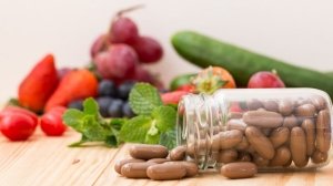 Glass jar of multivitamin capsules with fresh fruits and vegetables